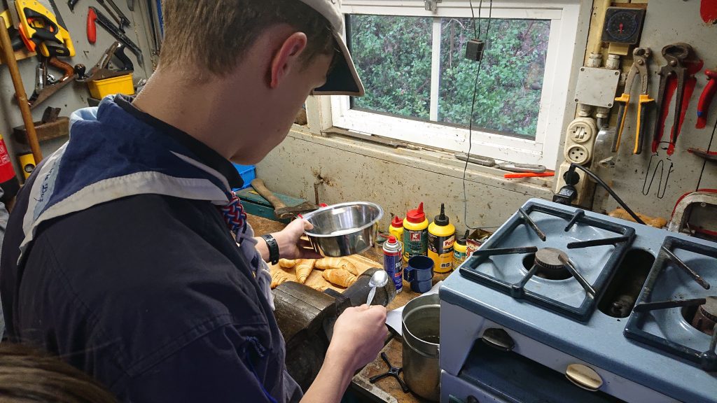 Scout of zeeverkenner, waterscout is in het kabelgat bezig met het voorbereiden van romige puddingcroissantjes.