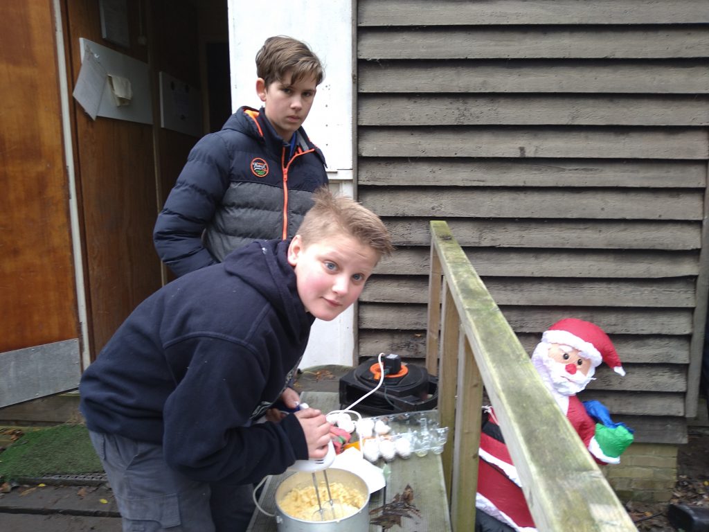 Kokende scouts en zeeverkenners en waterscouts bereiden pudding voor  buiten het clubhuis